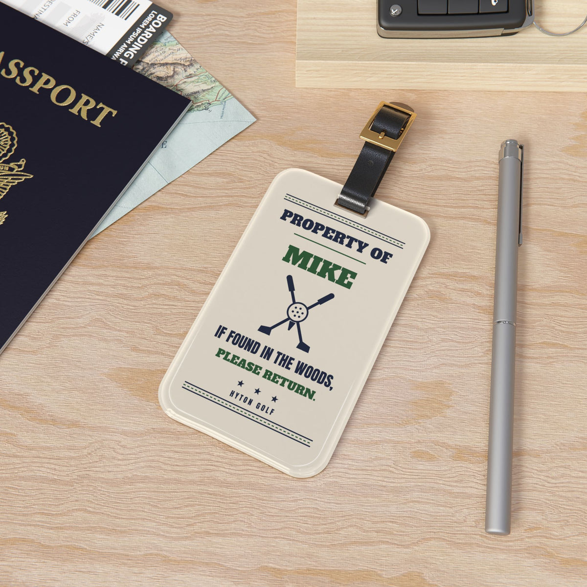 Property Of golf bag tag with leather strap on a desk next to a passport and pen
